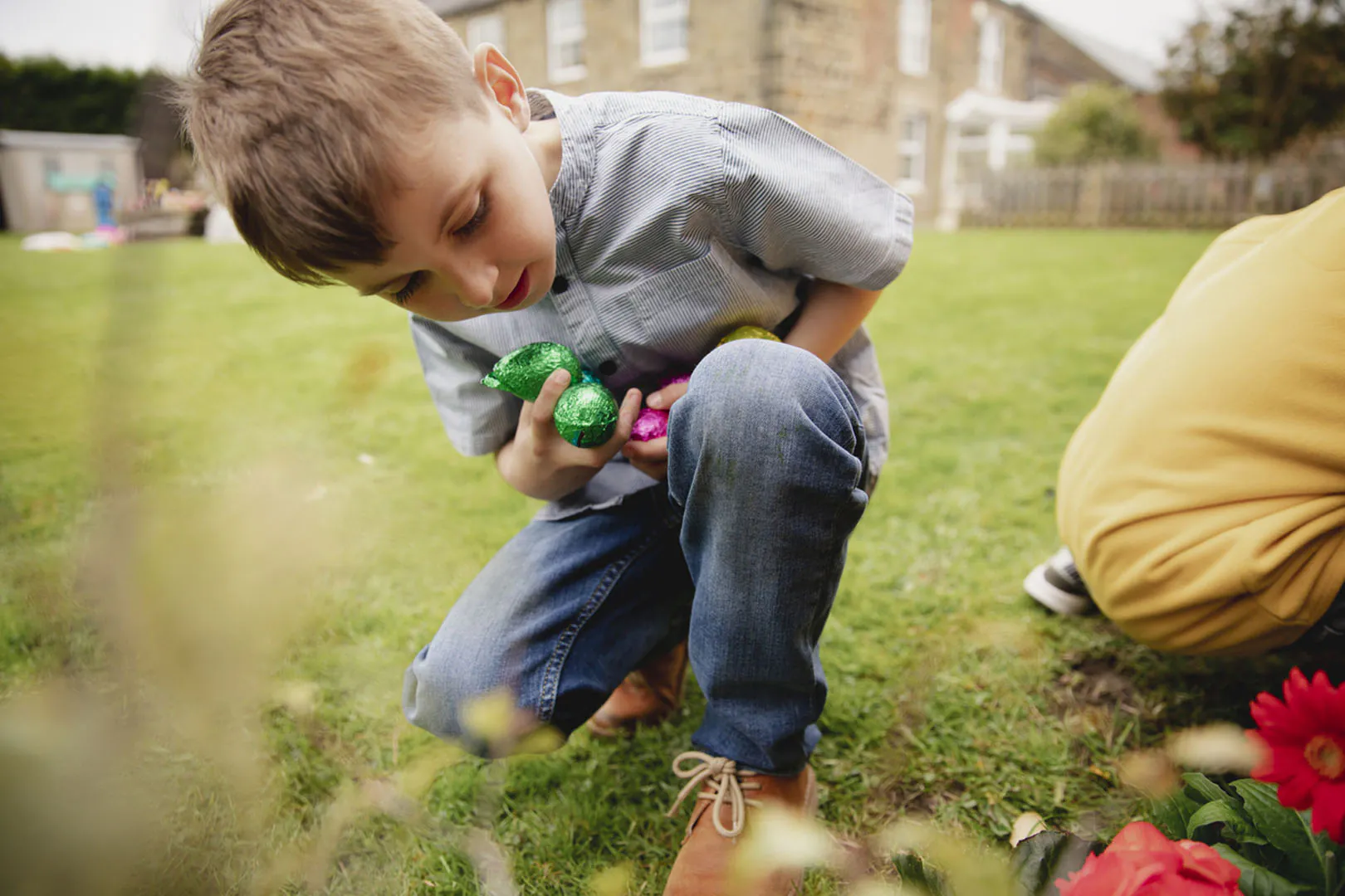 A young boy kneels in the grass, focused on Easter eggs during an Easter egg hunt in Cornwall.