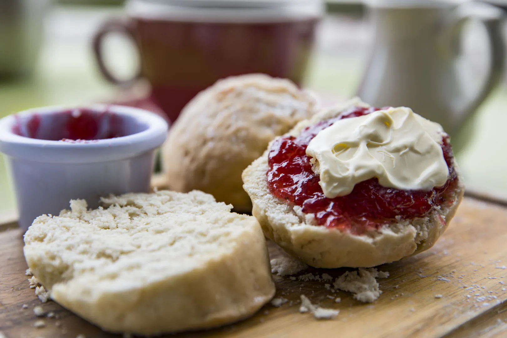 A freshly baked scone topped with jam and clotted cream, resting on a wooden cutting board.