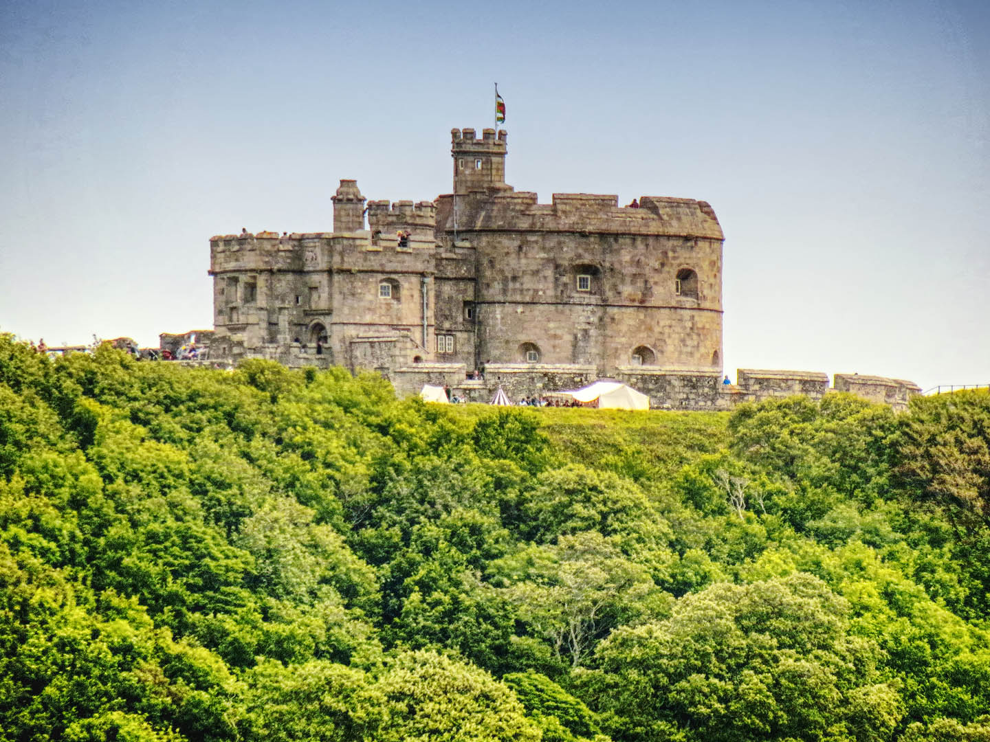 Pendennis Castle, in Falmouth, on a hillside with dense green foliage and a clear blue sky, a grand historic site in Cornwall.