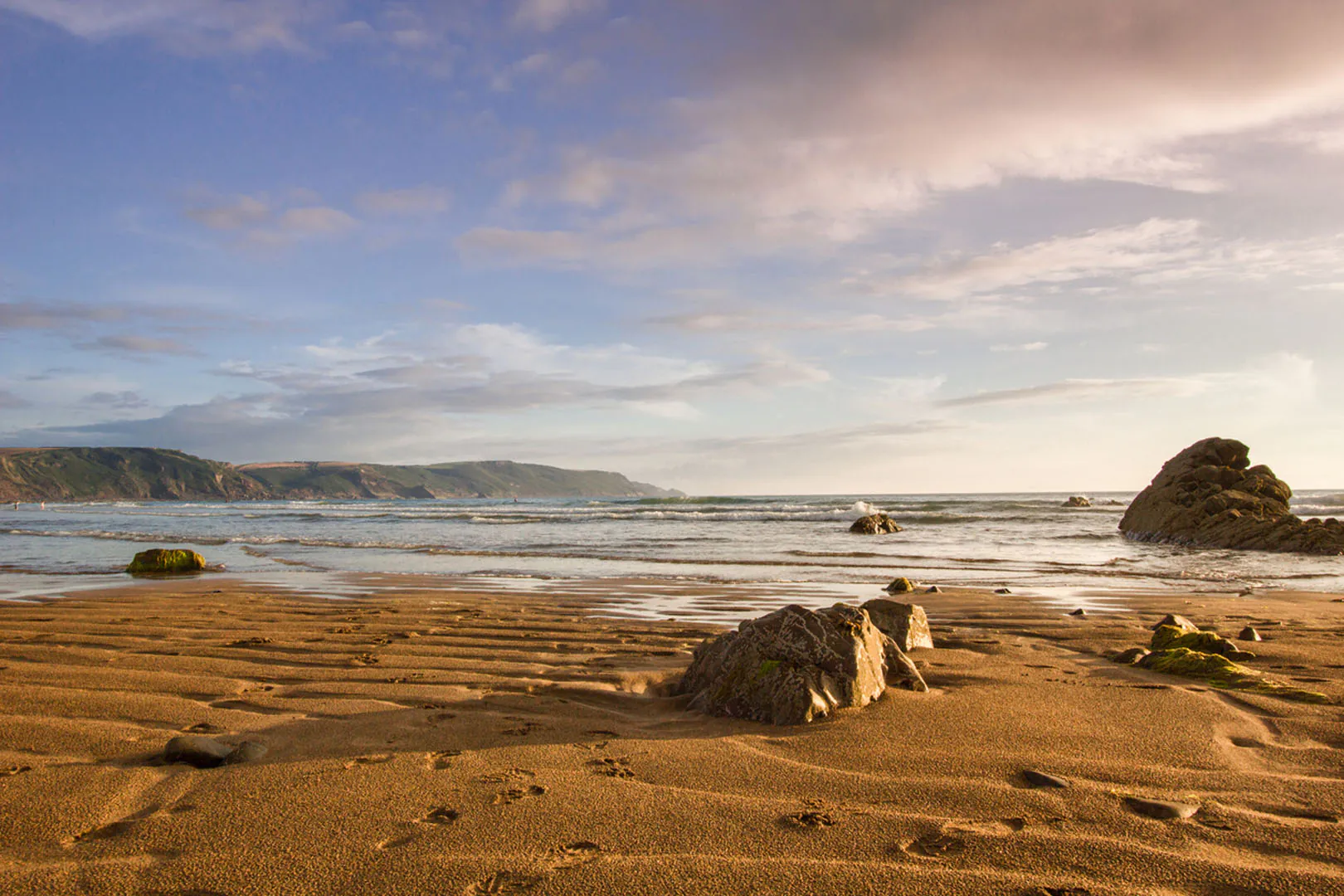 Scenic view of Widemouth Bay's sandy beach with rocks and water, ideal for exploring Cornwall's walking routes.