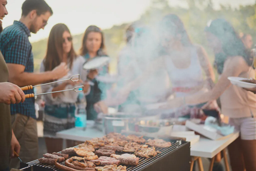 Group of people standing around grill.