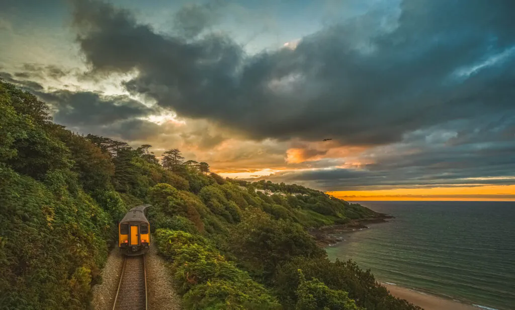 Scenic view of train moving through rugged coastal area in evening at sunset; sunset sky in background