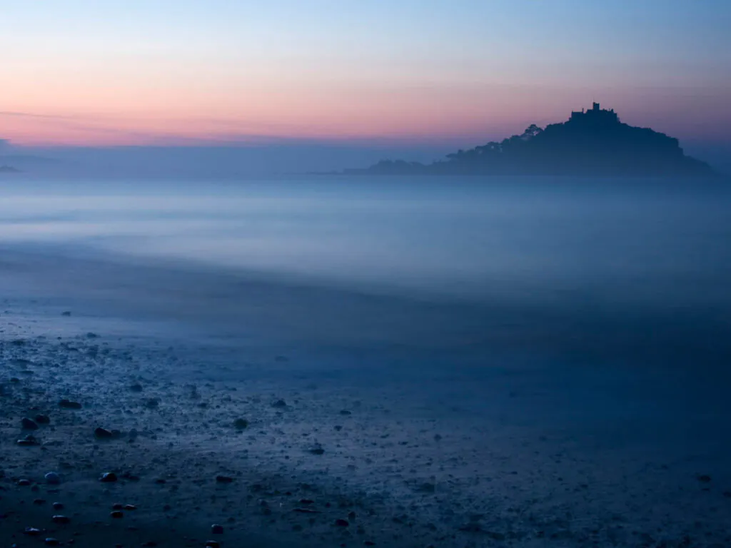 Long exposure photo of a sunset over a beach in Cornwall, featuring St Michael's Mount near Marazion in the background, a great place to visit from a Cornwall holiday cottage.